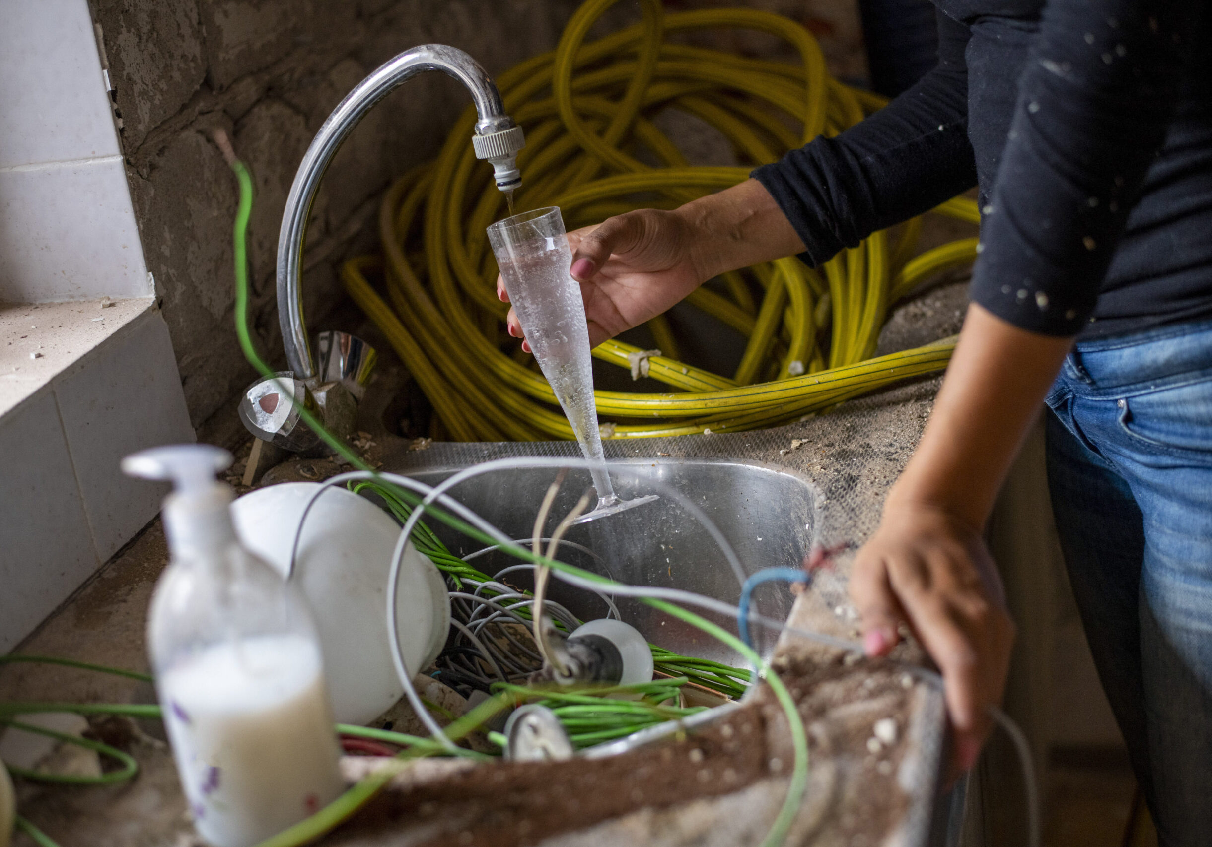 Person filling a glass with water at a cluttered sink.